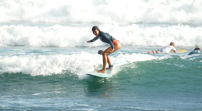 A beginner surfer grins mid-wave, arm out for balance, riding toward the beach