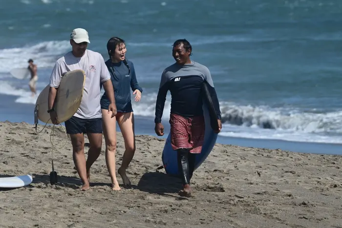 A coach and two students laughing together on the beach after a lesson