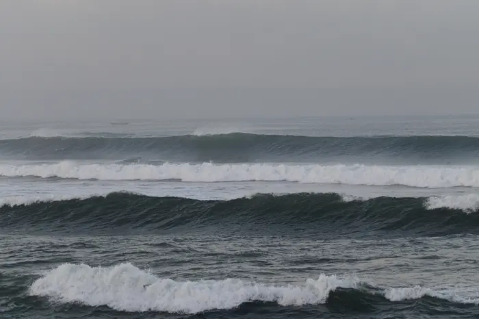 Empty, overcast lineup with several lines of swell peeling toward the sand