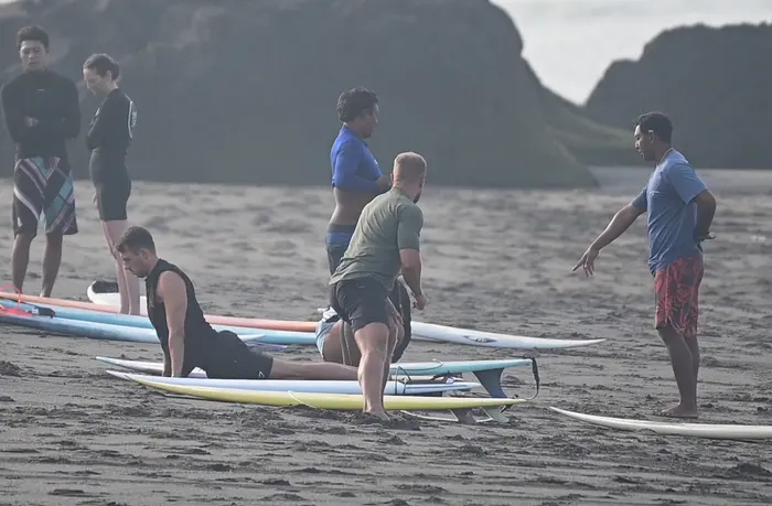 Students practice their pop-up technique on surfboards laid out on the sand while a coach guides them