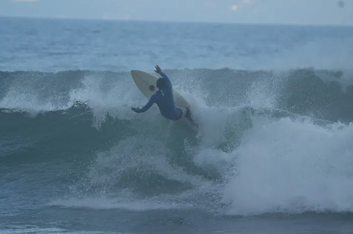 A surfer carves a sharp cutback in moody dusk light, spray flying off the wave