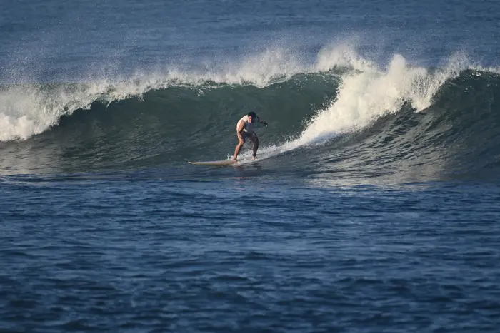 A surfer crouches low, dropping into a hollow, curling green wave