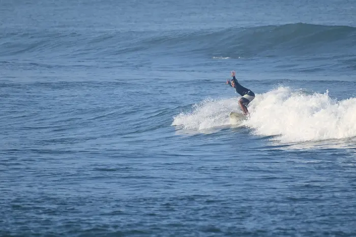 A surfer throws his arms up in celebration while riding a bright blue wave